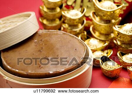 Stock Image - Chinese rice cake by bowls full of gold coins, close-up. Fotosearch