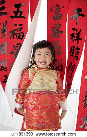 Stock Photo - Girl in Chinese traditional clothes with red envelopes standing, Calligraphy in the background. Fotosearch
