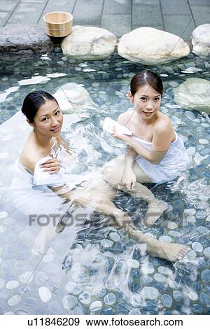 Stock Photo - Elevated view of young women sitting at hot spring. Fotosearch