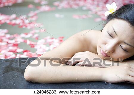 Stock Image - Young woman in pool with rose petals, resting. Fotosearch