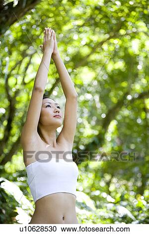 Stock Image - Young woman raising arms up in woods. Fotosearch