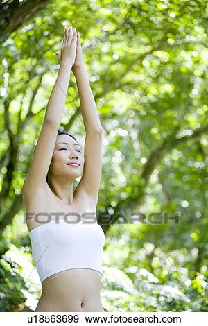 Stock Photo - Young woman raising arms up in woods with eyes closed. Fotosearch