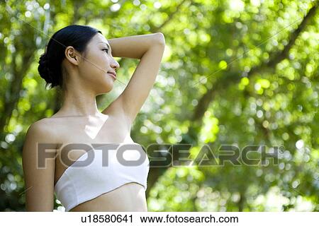 Stock Image - Young woman standing in woods, posing, looking away. Fotosearch