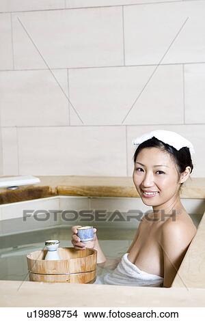 Picture - Young woman with towel on head, bathing in tub. Fotosearch