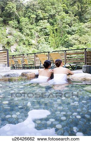 Stock Image - Young women with towel bathing in hot spring, rear view. Fotosearch