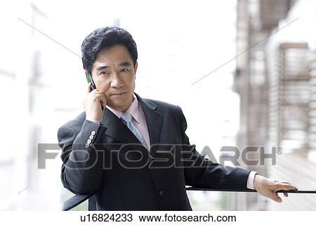 Stock Image - Businessman leaning against railing on the phone. Fotosearch