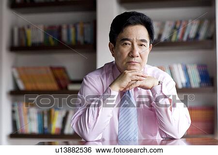 Businessman leaning on desk with hands on chin in office View Large Photo Image Stock Photograph - Businessman leaning on desk with hands on chin in office. Fotosearch