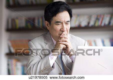 Stock Photography - Businessman looking at laptop, bookshelf in the background. Fotosearch