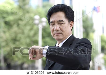 Stock Image - Businessman looking at watch outdoors. Fotosearch