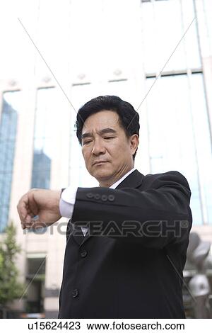 Stock Image - Businessman looking at watch outdoors. Fotosearch