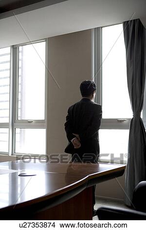 Picture - Businessman looking through window in office. Fotosearch