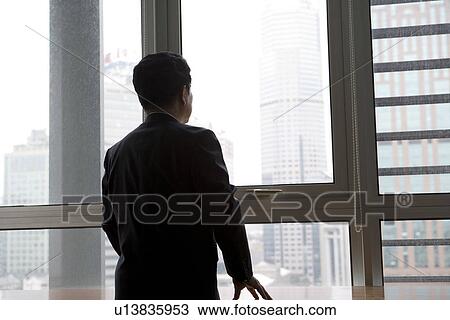 Stock Image - Businessman looking through window, rear view. Fotosearch