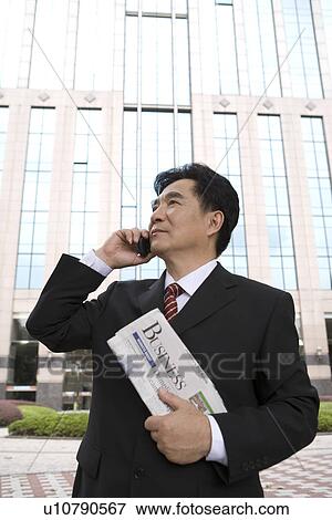 Stock Photo - Businessman on the phone holding newspaper by office building. Fotosearch