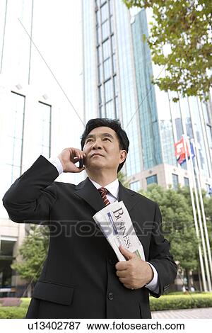 Stock Photo - Businessman on the phone holding newspaper, office building in the background. Fotosearch
