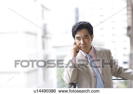Businessman on the phone leaning against railing, building in the background View Large Photo Image Stock Photograph - Businessman on the phone leaning against railing, building in the background. Fotosearch