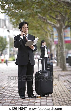 Stock Photo - Businessman on the phone with suitcase outdoors. Fotosearch