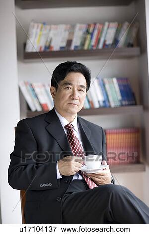 Stock Photo - Businessman sitting on chair holding a cup of coffee. Fotosearch