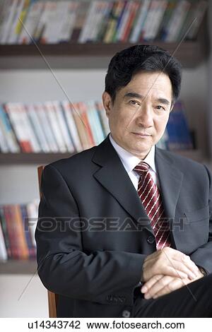 Stock Image - Businessman sitting on chair looking at camera in office. Fotosearch