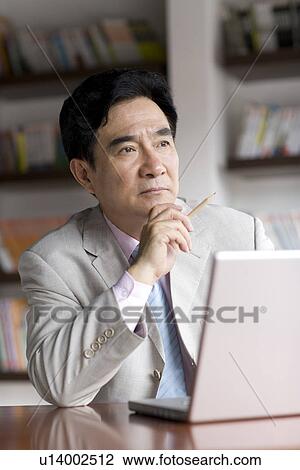 Businessman sitting on chair thinking with laptop on desk in office View Large Photo Image Stock Image - Businessman sitting on chair thinking with laptop on desk in office. Fotosearch