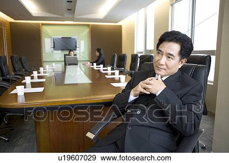 Stock Photo - Businessman sitting on chair, two businesswomen discussing in boardroom. Fotosearch