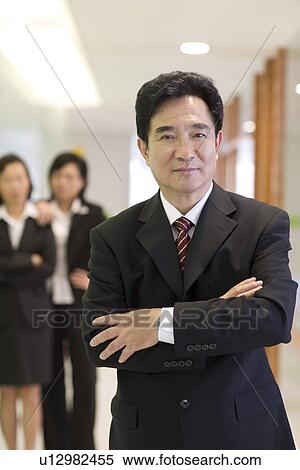 Businessman with arm crossed, two businesswoman in the background View Large Photo Image Stock Photography - Businessman with arm crossed, two businesswoman in the background. Fotosearch