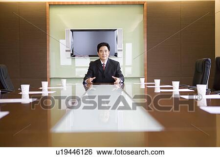 Stock Photograph - Man sitting alone in a boardroom. Fotosearch
