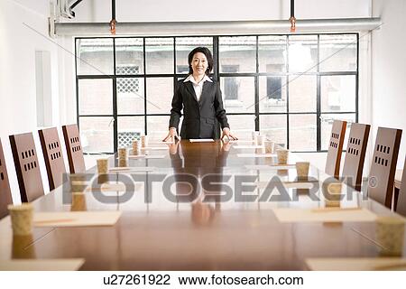 Stock Image - Businesswoman at head of table in boardroom. Fotosearch