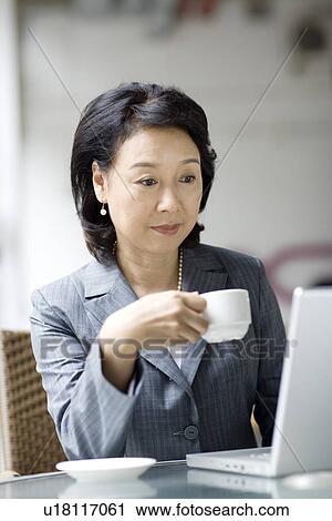 Businesswoman drinking coffee while looking at laptop View Large Photo Image Stock Image - Businesswoman drinking coffee while looking at laptop. Fotosearch