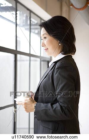 Businesswoman holding a cup of coffee standing by window View Large Photo Image Stock Image - Businesswoman holding a cup of coffee standing by window. Fotosearch