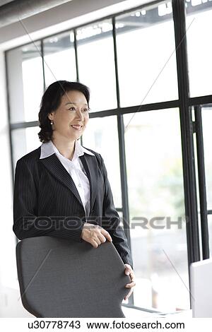 Stock Image - Businesswoman leaning on chair by window. Fotosearch