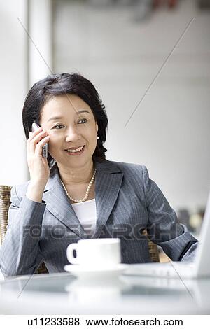 Stock Photo - Businesswoman on the phone with coffee cup and laptop on table. Fotosearch