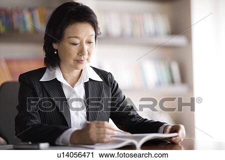 Stock Image - Businesswoman reading book in office. Fotosearch