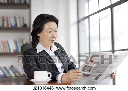 Businesswoman reading newspaper in office View Large Photo Image Stock Photograph - Businesswoman reading newspaper in office. Fotosearch