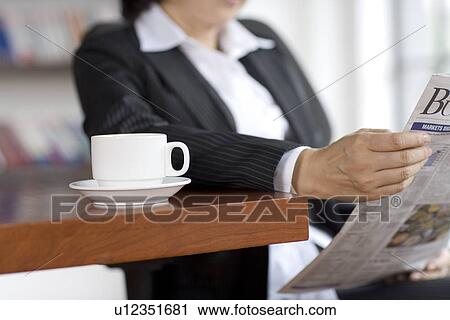 Stock Image - Businesswoman reading newspaper, mid section. Fotosearch