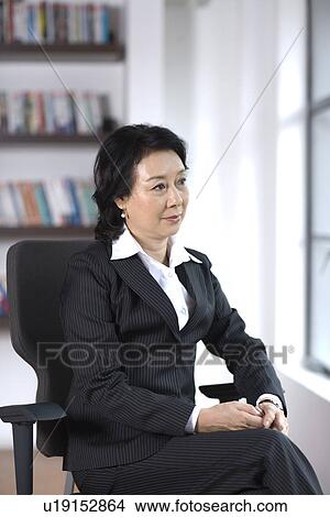Businesswoman sitting on chair by window in office View Large Photo Image Picture - Businesswoman sitting on chair by window in office. Fotosearch