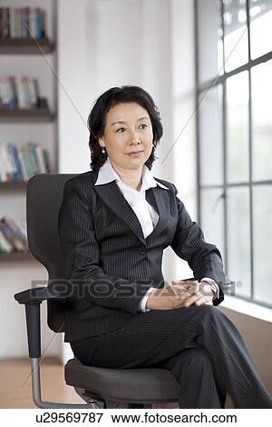 Businesswoman sitting on chair by window View Large Photo Image Stock Photo - Businesswoman sitting on chair by window. Fotosearch