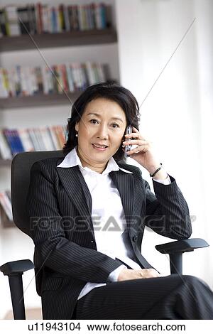 Picture - Businesswoman sitting on chair on the phone in office. Fotosearch