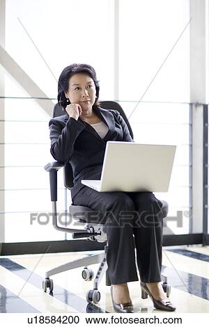Stock Image - Businesswoman sitting on chair with laptop. Fotosearch