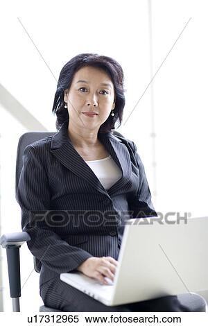 Stock Photography - Businesswoman sitting on chair with laptop in office. Fotosearch
