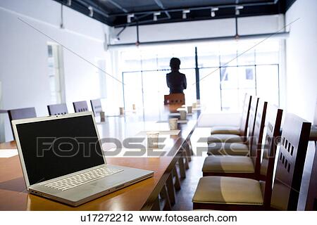 Businesswoman standing by window, rear view, laptop on conference table in the foreground View Large Photo Image Stock Image - Businesswoman standing by window, rear view, laptop on conference table in the foreground. Fotosearch