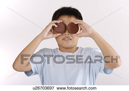 Stock Photo - Boy holding two biscuits over eyes, close-up. Fotosearch