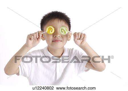 Stock Image - Boy holding two lollipops over eyes, close-up. Fotosearch