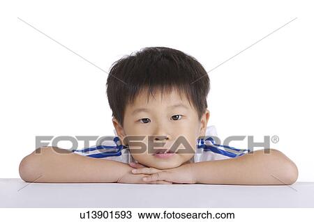 Stock Image - Boy leaning on table, smiling, portrait, close-up. Fotosearch