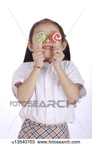 Stock Image - Girl (6-7) holding two Lollipop over eyes, close-up. Fotosearch