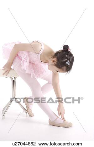 Stock Image - Ballet dancer sitting on stool touching her foot, portrait. Fotosearch