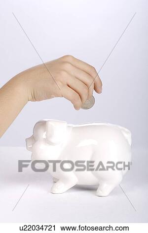 Stock Image - Boy holding coin over piggy bank. Fotosearch