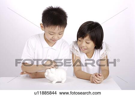 Picture - Boy putting coin into piggy bank, girl looking and smiling. Fotosearch