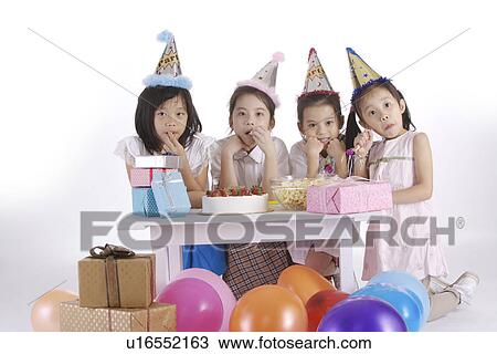 Stock Image - Four girl kneeling by table, gifts and balloons aside. Fotosearch