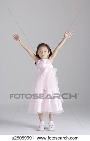 Stock Image - Girl wearing dress with arms raised, portrait. Fotosearch