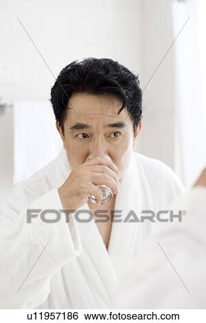 Stock Photograph - Senior man drinking water in bathroom. Fotosearch
